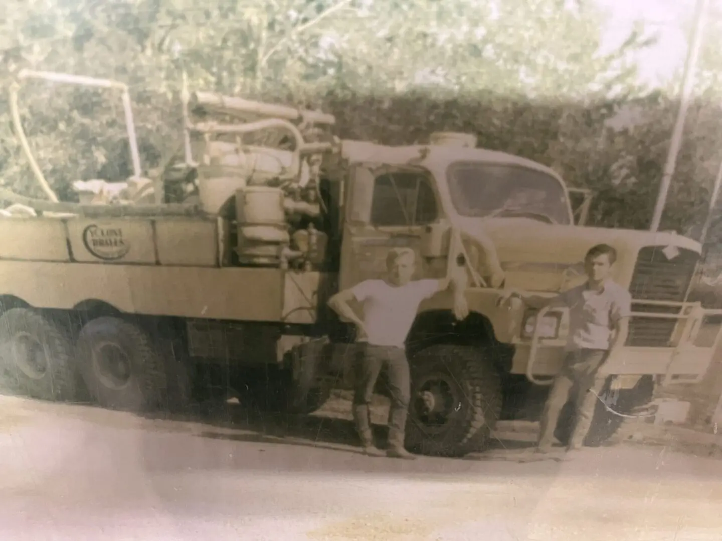 An old photo of two men posing by a big truck