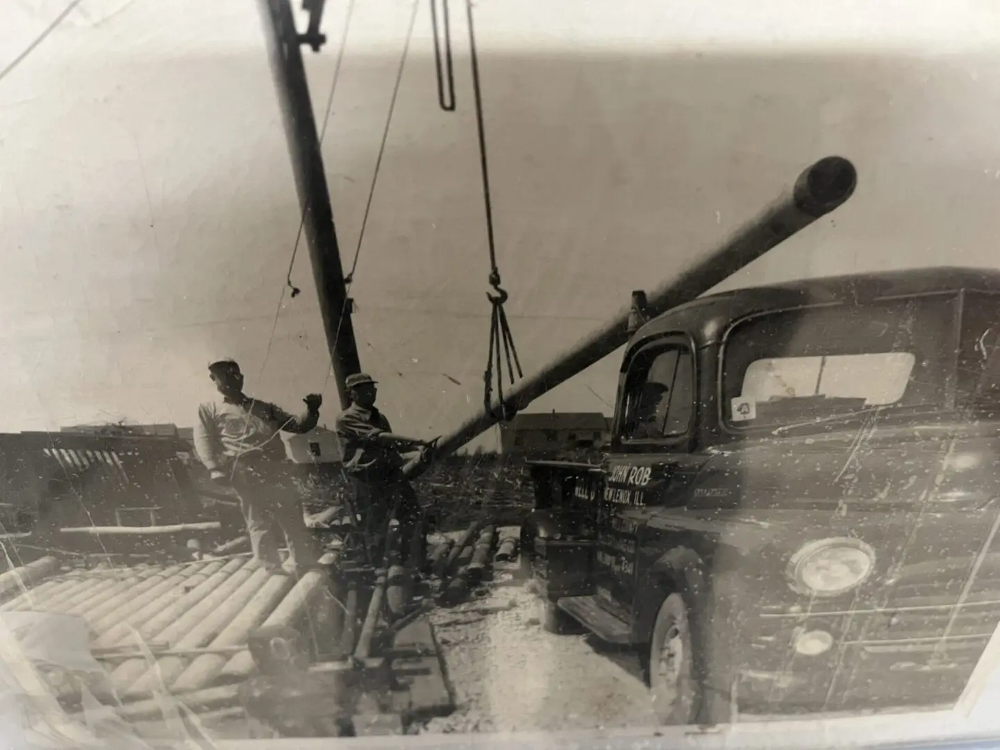An old photo of two men with a large pipe and a vintage car